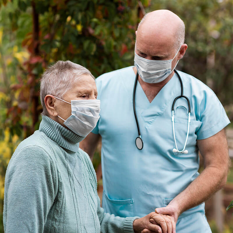 oudere vrouw wordt geholpen door verpleger, beiden met mondkapjes